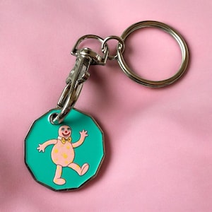 May include: A novelty keychain featuring a cartoon character. The teal-coloured charm has a pink character with yellow spots and a bow tie. The keychain has a silver clasp and a large silver ring.