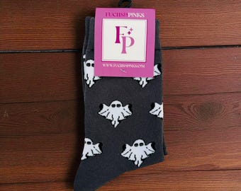 Puede incluir: Calcetines gris oscuro con un patrón repetido de fantasmas blancos de dibujos animados. Los calcetines tienen una etiqueta rosa con el texto "FUCHSIA PINKS" y una dirección web. Los calcetines se muestran sobre una superficie de madera.