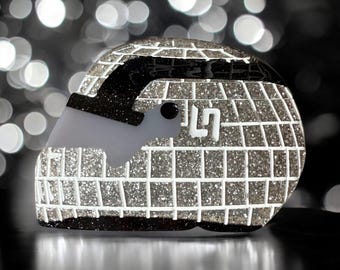 Puede incluir: Un casco plateado con purpurina, un patrón de rejilla blanca y una visera negra. El casco tiene el número "9" en el lateral. Es un objeto decorativo.