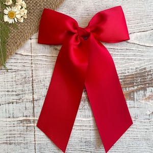 Puede incluir: Un gran lazo rojo brillante hecho de cinta de grosgrain. El lazo está atado con colas largas y es perfecto para agregar un toque festivo a cualquier ocasión.