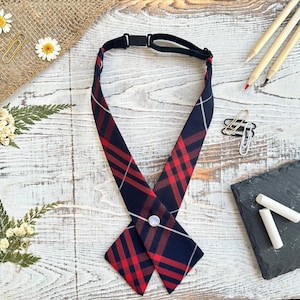 Könnte beinhalten: Eine rot-schwarze karierte Krawatte mit weißem Akzent und Druckknopfverschluss. Die Krawatte liegt flach auf einer Holzoberfläche.