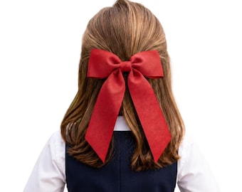 May include: A large, solid red hair bow with two long, pointed tails attached to the back of light brown hair. The bow is centered at the crown of the head, featuring a smooth, matte texture and a classic shape with a central knot detail.
