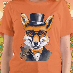 Puede incluir: Camiseta naranja con un zorro estilizado que lleva un sombrero de copa, gafas y una pajarita. El zorro viste un traje y la palabra "fantastic" está escrita en cursiva debajo.