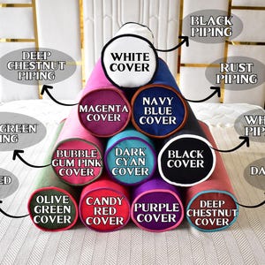 May include: A collection of cylindrical pillows in various colors, including magenta, navy blue, and black. Each pillow features a different colored cover and piping, with labels indicating the color names. The pillows are arranged in a pyramid shape.