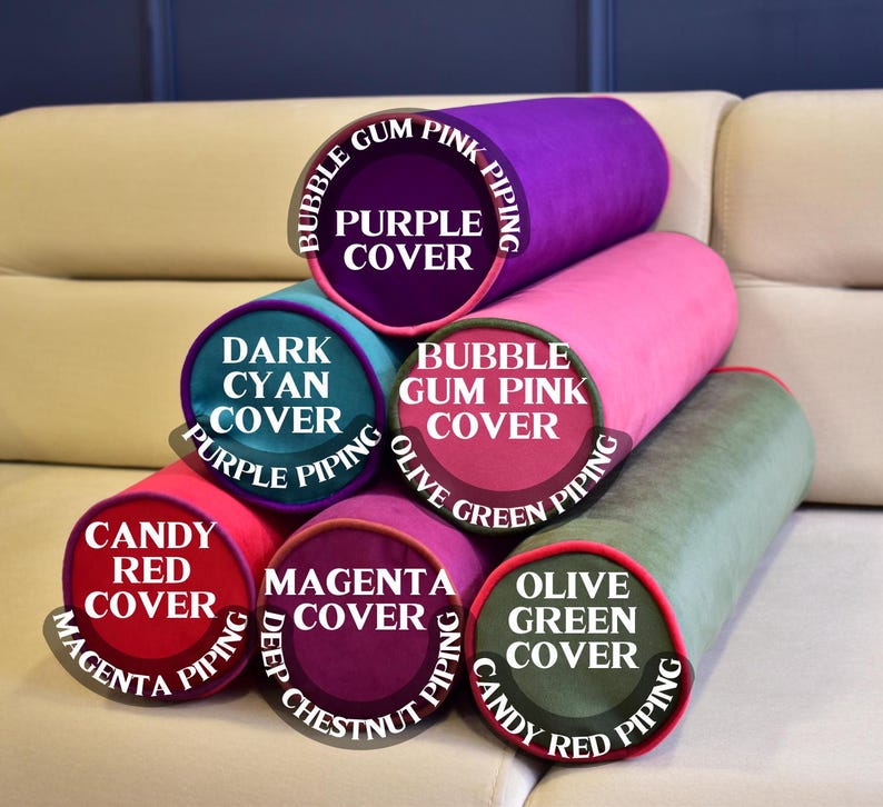 May include: A stack of cylindrical pillows in various colors, including purple, pink, green, and red. Each pillow has a contrasting color piping and a label indicating the cover and piping colors. The pillows are arranged on a beige sofa.