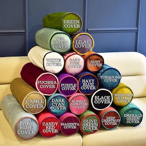 May include: A display of cylindrical pillows in various colors, including green, purple, and blue. Each pillow has a different color cover, with text labels such as "Sea Green Cover" and "Baby Pink Cover". The pillows are stacked on a cream-colored sofa.