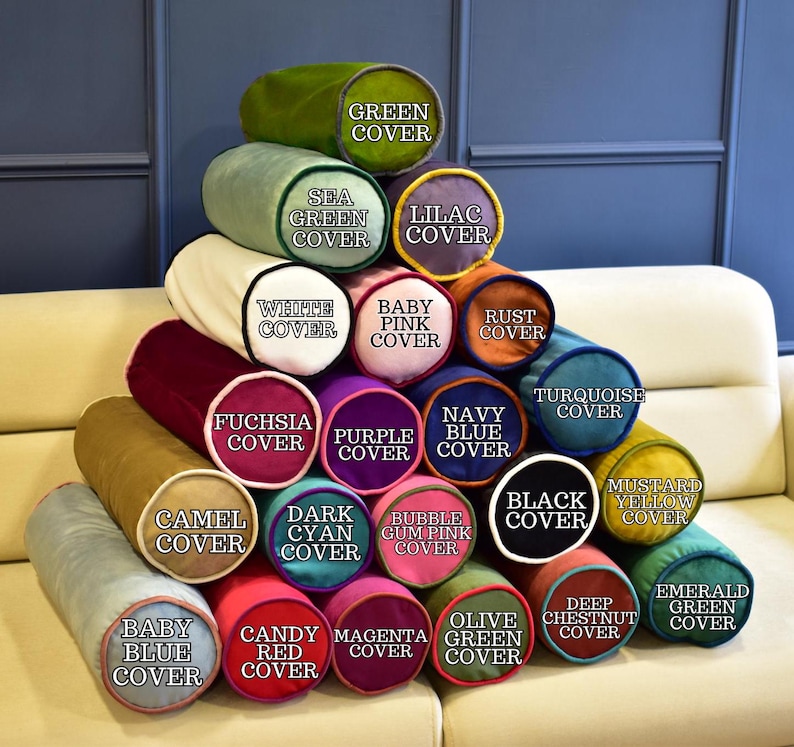 May include: A display of cylindrical pillows in various colors, including green, purple, and blue. Each pillow has a different color cover, with text labels such as "Sea Green Cover" and "Baby Pink Cover". The pillows are stacked on a cream-colored sofa.
