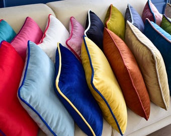 May include: A collection of decorative throw pillows in various colors and textures. The pillows are arranged in a row on a white couch. The pillows have a variety of colors, including teal, pink, white, blue, yellow, orange, and brown. The pillows have a contrasting trim around the edges.