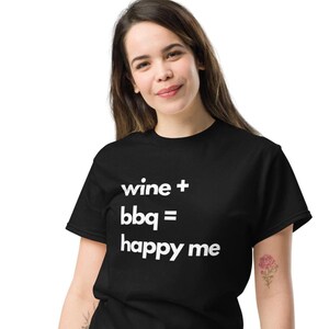 May include: Black t-shirt with the white text "wine + bbq = happy me". The shirt is made of a soft material and has a classic crew neck design. The shirt is a casual wear item.