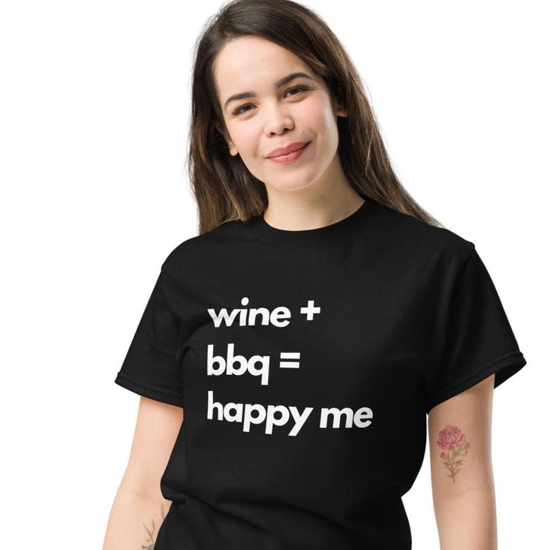 May include: Black t-shirt with the white text "wine + bbq = happy me". The shirt is made of a soft material and has a classic crew neck design. The shirt is a casual wear item.
