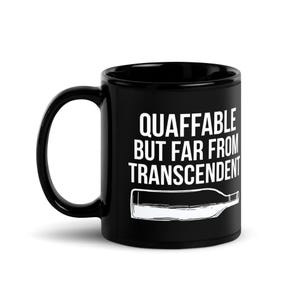 May include: Black ceramic coffee mug with the text "QUAFFABLE BUT FAR FROM TRANSCENDENT" in white. A white illustration of a wine bottle is below the text. The mug has a curved handle.