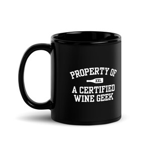 Puede incluir: Taza de café de cerámica negra con texto blanco que dice "PROPERTY OF A CERTIFIED WINE GEEK" con un pequeño gráfico de botella de vino y la palabra "XXL" encima.