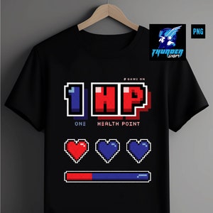 Pode incluir: Camiseta preta com um gráfico pixelado de "1 HP" com o texto "One Health Point" abaixo. O gráfico também inclui três corações pixelados e uma barra de progresso.