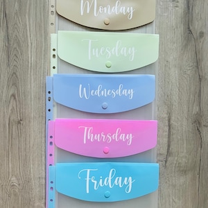 May include: Five clear plastic folders with different coloured fronts and white text. The folders are labelled Monday, Tuesday, Wednesday, Thursday, and Friday.