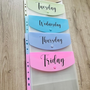 May include: A set of five clear plastic folders with coloured pockets labelled "Monday", "Tuesday", "Wednesday", "Thursday", and "Friday".