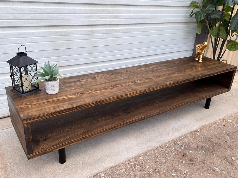 May include: A dark brown wooden media console with a shelf and black metal legs. The console is sitting on a concrete floor.