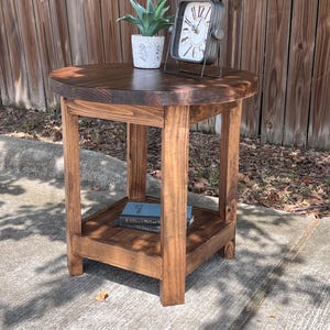 May include: A dark stained wooden side table with a round top and a lower shelf. A small potted plant and a vintage-style clock are displayed on the table. The table is approximately 24 inches tall.