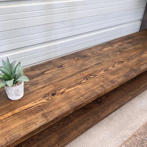 May include: A dark brown wooden coffee table with a lower shelf. The table has a natural wood grain finish and is made of reclaimed wood.