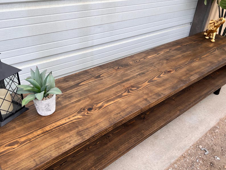 May include: A dark brown wooden coffee table with a lower shelf. The table has a natural wood grain finish and is made of reclaimed wood.