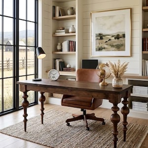 May include: A dark wood desk with turned legs, a brown leather office chair, a black desk lamp, a round analog clock, a gold wire globe, and a ceramic vase with dried pampas grass, all arranged on a textured rug in a home office space.