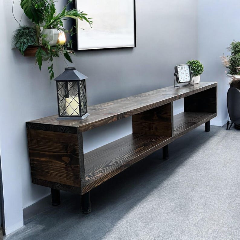 May include: A dark brown wooden media console with three open shelves and black metal legs. The console is 60 inches long and 16 inches deep.