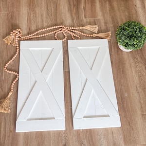 May include: Two white wooden doors with an X-shaped design. The doors are closed and have a rustic look.