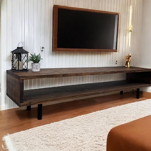 May include: A dark wood TV stand with two shelves and black metal legs. The stand is in front of a white wall with a flat screen TV mounted above it.