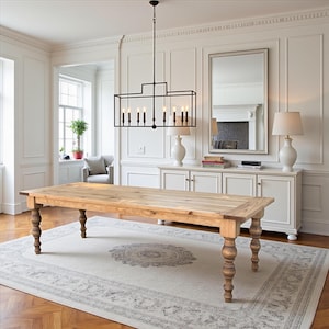 May include: A rectangular wooden dining table with a natural light brown finish and four turned, spindle-style legs. The table is positioned in a room with a large black metal rectangular chandelier hanging above it, featuring eight vertical light bulbs.