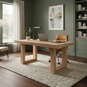 May include: A rectangular light oak desk with a thick top and U-shaped legs. The desk holds a silver laptop, a small potted green plant, and a desk lamp. A tan leather office chair with wheels is positioned at the desk on a textured cream rug.