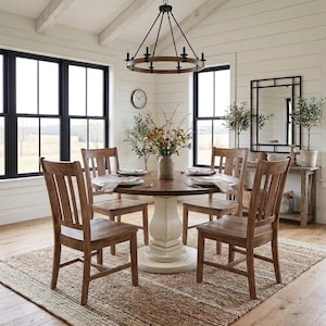 May include: A round wooden dining table with a white pedestal base, surrounded by four wooden chairs with slatted backs. A circular chandelier with black metal accents hangs above the table, which is set with plates and a central floral vase.