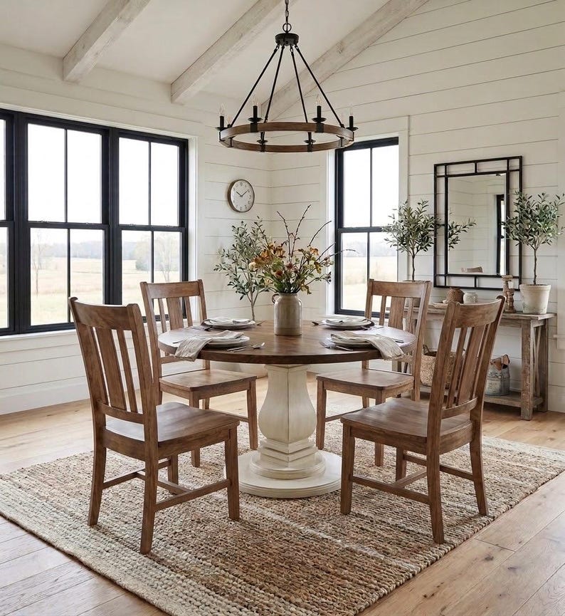 May include: A round wooden dining table with a white pedestal base, surrounded by four wooden chairs with slatted backs. A circular chandelier with black metal accents hangs above the table, which is set with plates and a central floral vase.