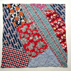 May include: A square quilted fabric piece featuring a patchwork of diagonal panels. Patterns include orange floral prints, navy blue stripes with small pink flowers, red floral motifs, teal geometric bands, red gingham, and light blue swirls.