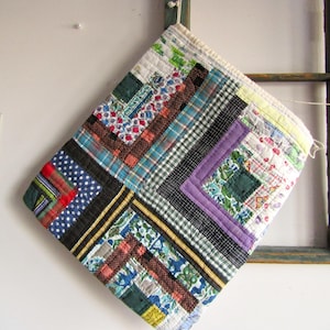May include: A handmade, quilted potholder with a patchwork design. The potholder features a variety of fabrics in blue, green, red, and purple, arranged in a log cabin pattern. The potholder is square and has a loop for hanging.