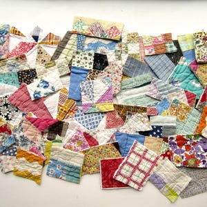 May include: A collection of small, irregularly shaped fabric patches in various colors and patterns. The patches include floral, geometric, and solid designs, with a quilted texture. The arrangement is scattered, creating a patchwork effect.