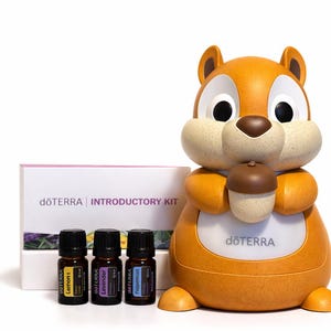 May include: An orange and tan squirrel-shaped essential oil diffuser holds a brown acorn. Three small essential oil bottles and a box labelled "dōTERRA INTRODUCTORY KIT" are next to the diffuser. The bottles are labelled "Lemon", "Lavender", and "Peppermint".