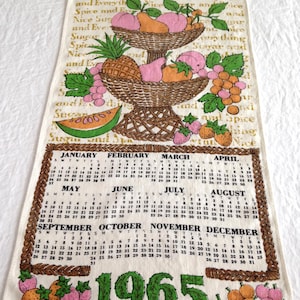 May include: A cream-colored fabric calendar towel for the year 1965. The top features a basket of fruit and the text Sugar and Spice and Everything Nice. The bottom displays the twelve months of the year in a brown border with green 1965 text.