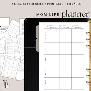 May include: A black and gold planner with the text "MOM LIFE planner" printed on the cover. The planner has a weekly layout with columns for Monday, Tuesday, and Wednesday. There are sections for "Personal", "Kids", "Home", "Friends", and "Out & About".