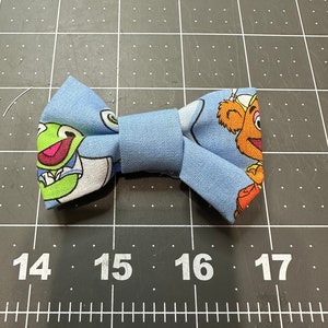 May include: A blue bow tie with a green frog and a brown bear on it.