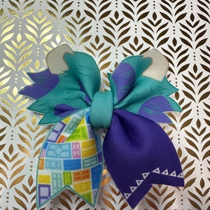 May include: A teal, purple, and yellow bow with a geometric pattern. The bow has a white center and is tied with a white ribbon.