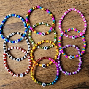 May include: A set of eight colourful beaded bracelets with letter charms. The bracelets are made with small, colourful beads and feature a letter charm in the centre of each bracelet. The letters spell out the word "SPEARIG".