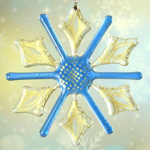 May include: A blue glass snowflake ornament with gold accents. The snowflake has a detailed design with a center of gold dots.