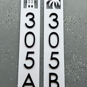 Puede incluir: Dos letreros verticales blancos con n&uacute;meros y letras negras. El letrero de la izquierda tiene una silueta de casa y el letrero de la derecha tiene una silueta de palmera. Los letreros dicen 305A y 305B.