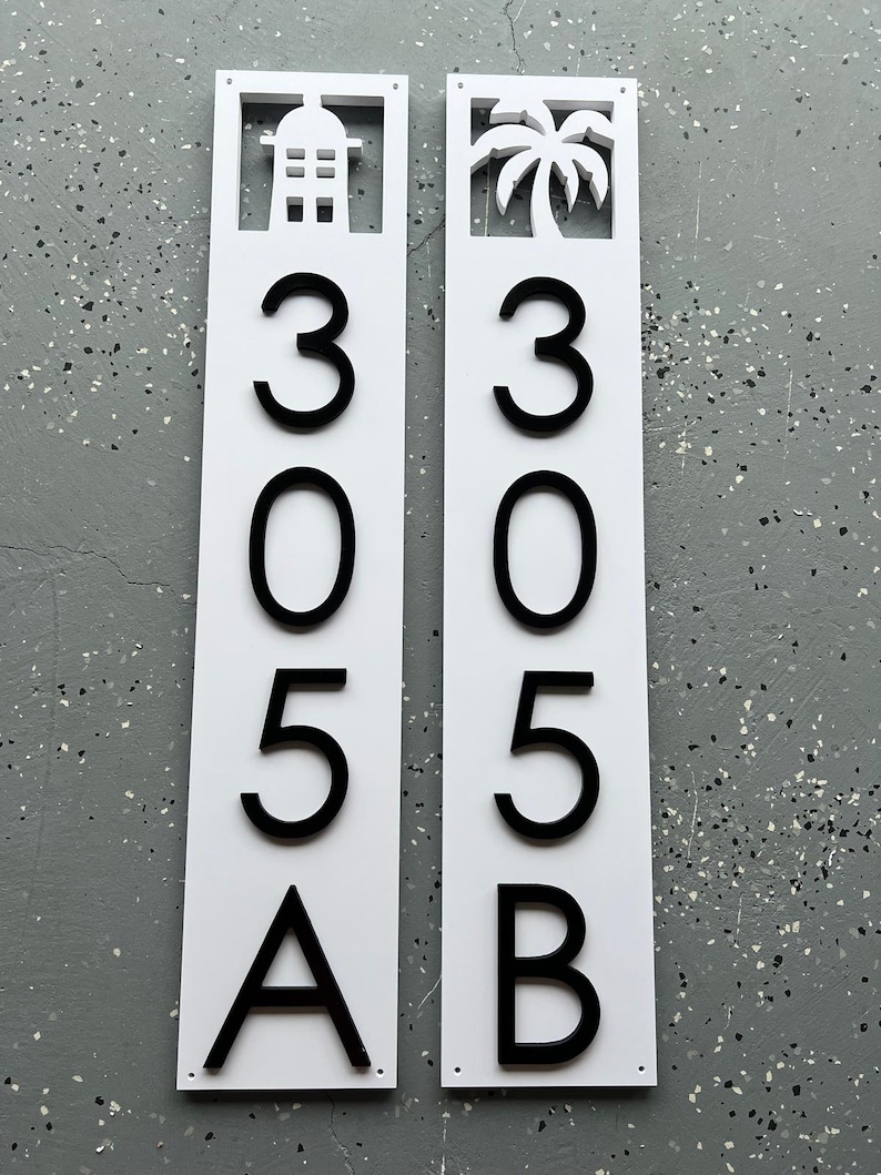 Puede incluir: Dos letreros verticales blancos con n&uacute;meros y letras negras. El letrero de la izquierda tiene una silueta de casa y el letrero de la derecha tiene una silueta de palmera. Los letreros dicen 305A y 305B.
