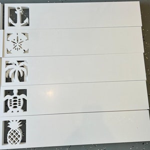 Puede incluir: Cinco placas de madera blanca con diferentes dise&ntilde;os recortados. Los dise&ntilde;os incluyen un ancla, una concha, una palmera, una tortuga y una pi&ntilde;a.
