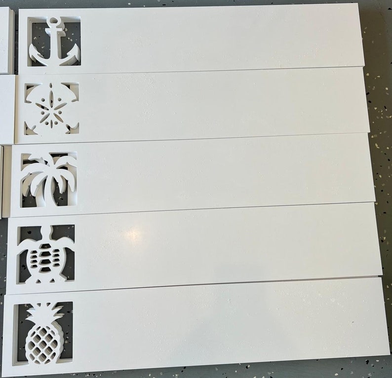 Puede incluir: Cinco placas de madera blanca con diferentes dise&ntilde;os recortados. Los dise&ntilde;os incluyen un ancla, una concha, una palmera, una tortuga y una pi&ntilde;a.