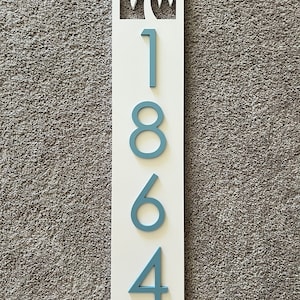 Puede incluir: Un letrero de madera blanco con un dise&ntilde;o de palmera recortada y n&uacute;meros pintados de azul 1864.