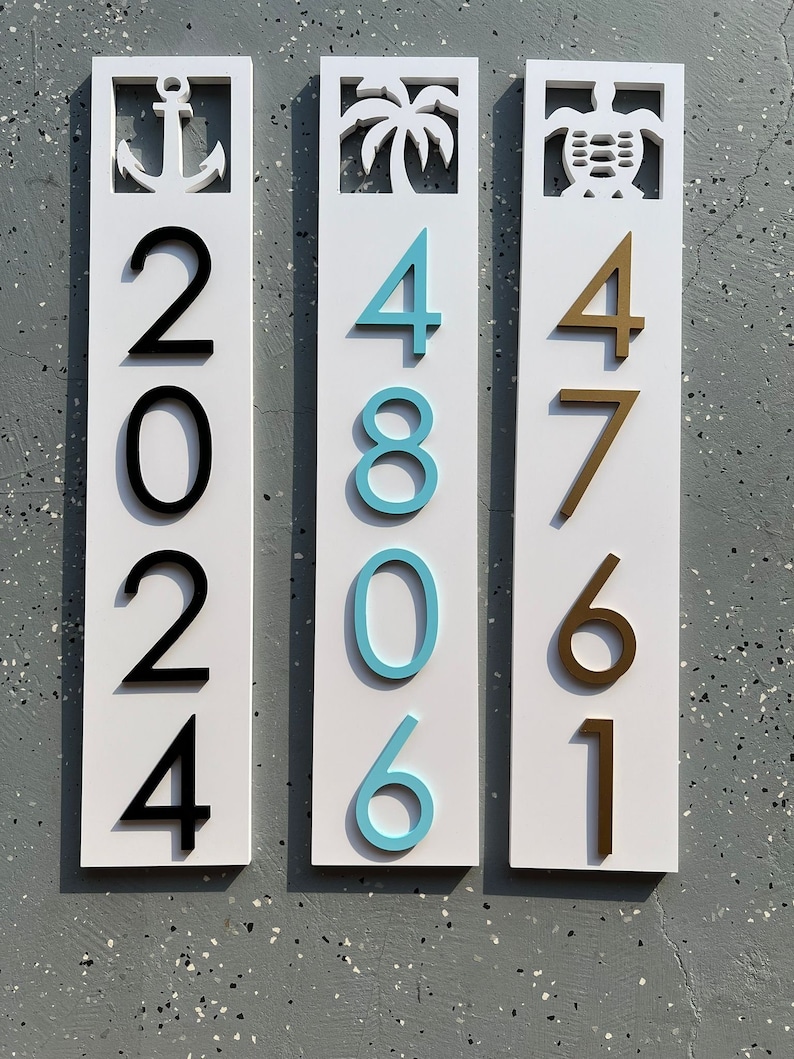 Puede incluir: Tres letreros de madera blanca con dise&ntilde;os recortados y n&uacute;meros negros, azules y dorados. El primer letrero tiene un dise&ntilde;o de ancla y los n&uacute;meros 2024. El segundo letrero tiene un dise&ntilde;o de palmera y los n&uacute;meros 4806. El tercer letrero tiene un dise&ntilde;o de tortuga y los n&uacute;meros 4761.