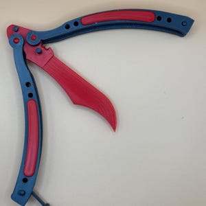 May include: A red and blue butterfly knife with a textured handle. The knife is open and the blade is visible.