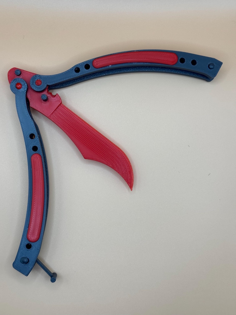 May include: A red and blue butterfly knife with a textured handle. The knife is open and the blade is visible.