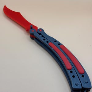 May include: A red and blue butterfly knife with a curved blade. The blade is open and the handle is closed.